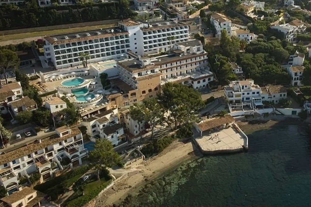Vista aérea de un complejo hotelero en la costa con piscinas y edificios blancos