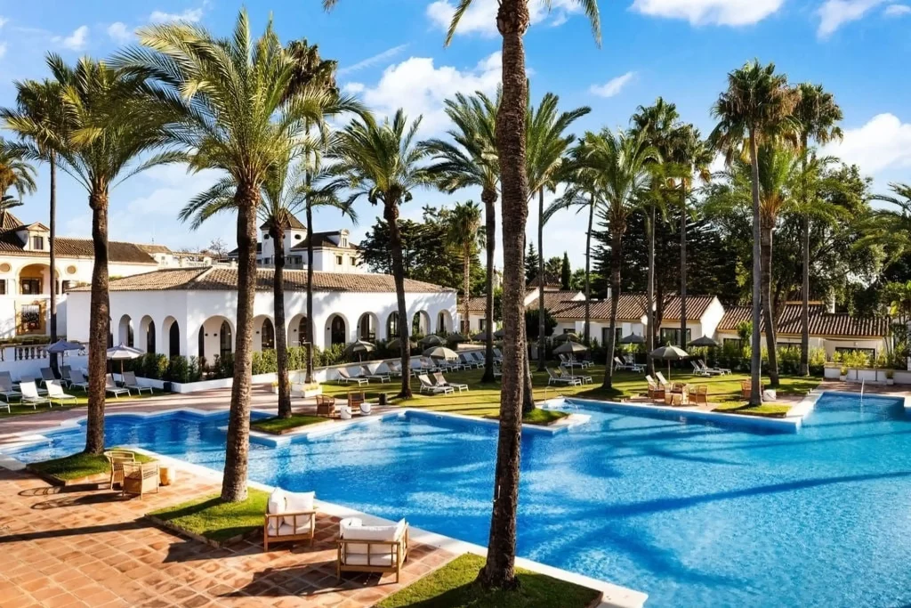 Piscina de hotel de lujo con palmeras y edificios blancos al fondo bajo un cielo azul