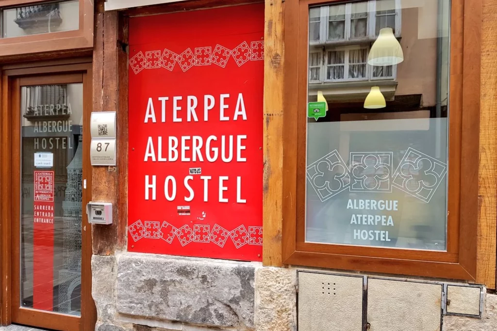 Entrada del Albergue Aterpea en la Catedral, con puerta de madera y ventana con cartel rojo