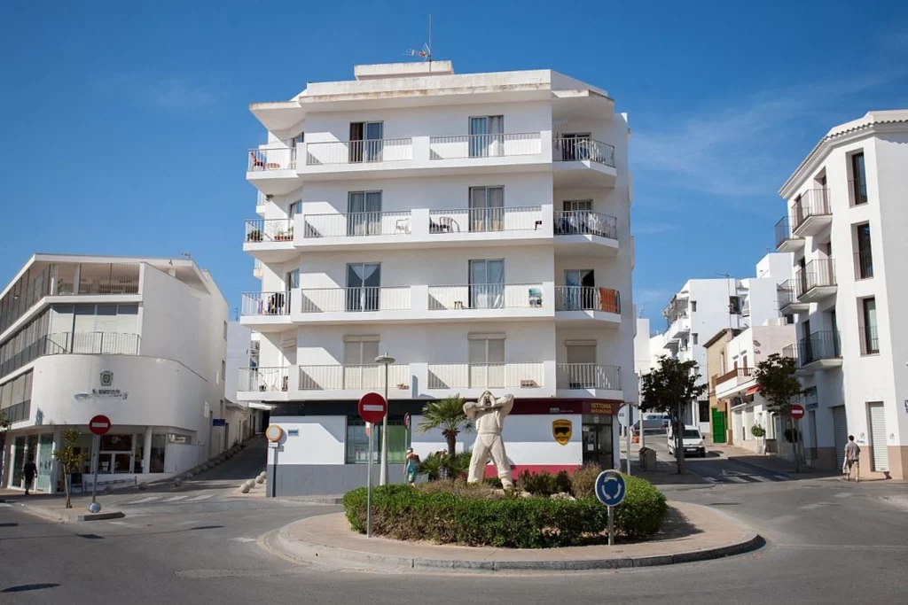 Vista de un hotel blanco en Ibiza con balcón y jardín en la entrada
